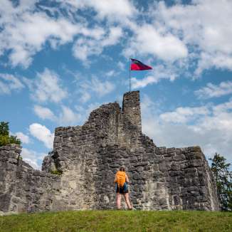 Randonneuse devant les ruines historiques du château de Schellenberg avec le drapeau du Liechtenstein flottant sous un ciel bleu