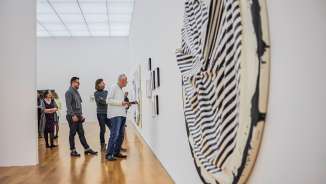 Les visiteurs contemplent des œuvres d'art moderne dans une galerie du Kunstmuseum Liechtenstein à l'architecture lumineuse et au sol en bois.