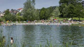 Journée estivale au bord du lac naturel du parc de loisirs de Grossabünt, entouré de prairies verdoyantes et d'arbres.