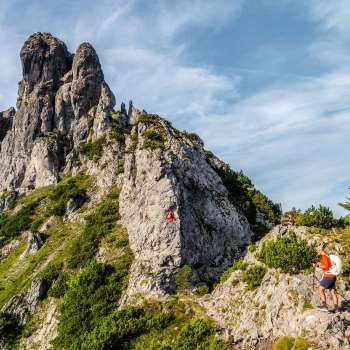 Randonneurs sur un sentier de montagne rocheux devant une arête déchiquetée avec un panneau de signalisation rouge et blanc