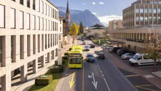 Un bus LIEmobil traverse Vaduz avec les Alpes en toile de fond et une architecture moderne.