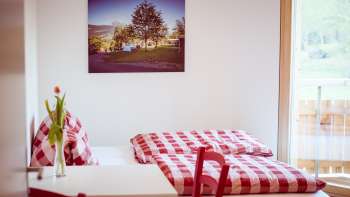 Chambre double confortable dans la maison d'hôtes près du camping Mittagsspitze avec des draps et une décoration à carreaux rouges et blancs.