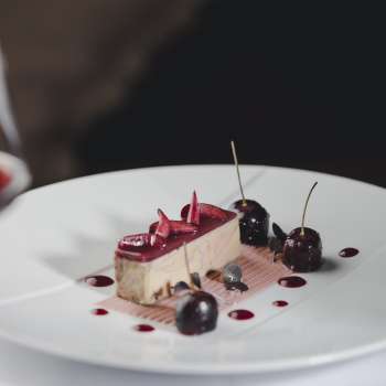 Dessert élégant sur une assiette blanche, décoré de cerises et de chocolat.