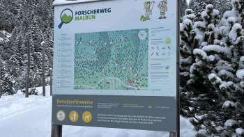 Fillette au chapeau vert regardant à travers un télescope sur le sentier des chercheurs de Malbun avec vue panoramique sur les Alpes liechtensteinoises.