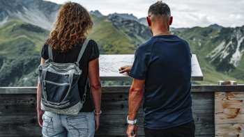 Un couple regarde le panneau d'information sur la terrasse de l'auberge de montagne Sareis.