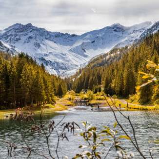 Ambiance automnale à Steg, Liechtenstein, avec des forêts colorées, un lac clair et des Alpes enneigées en arrière-plan