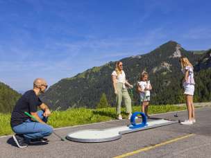 Une famille profite d'une partie de minigolf sous le soleil de Malbun, au Liechtenstein, entourée d'un paysage alpin verdoyant et de montagnes en été.