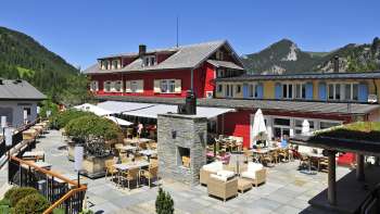 Vue extérieure du restaurant sous le soleil, avec une façade rouge et un panorama montagneux.