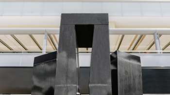 Sculpture "Progression d'une forme en 3 stèles" de Christian Megert en pierre noire devant une façade moderne en verre à Vaduz.