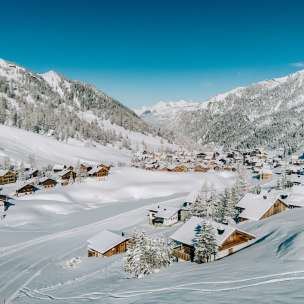 Vue aérienne de Malbun en hiver avec des maisons en bois enneigées, intégrées dans le paysage alpin du Liechtenstein.