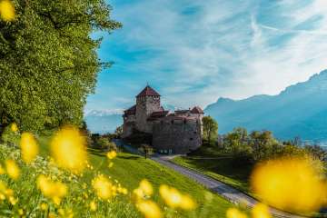 Le château de Vaduz entouré de prairies printanières en fleurs et de montagnes en arrière-plan - l'emblème du Liechtenstein dans toute sa splendeur