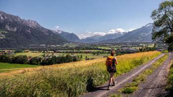 Une femme se promène sur un chemin de terre avec une vue panoramique sur la vallée du Rhin au Liechtenstein