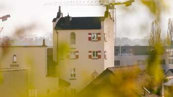 Gros plan sur la tour historique de l'hôtel de ville de Vaduz avec ses remarquables volets rouges, entourée de grues de chantier en arrière-plan.