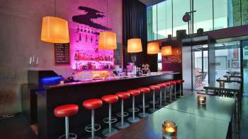Bar moderne avec un long comptoir, des tabourets de bar rouges et un éclairage stylé rose et orange