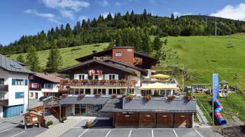 Vue extérieure du restaurant Turna près d'une pente verte avec une terrasse d'été et des plantes fleuries. Vue extérieure du restaurant Turna près d'une pente verte avec une terrasse d'été et des plantes fleuries.