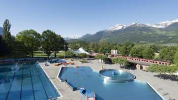 Vue générale de la piscine en plein air de Mühleholz avec plusieurs bassins et un magnifique panorama alpin en arrière-plan.