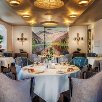 Tables dressées en rond avec verres à vin et bougies dans l'élégante salle à manger du Park Hotel Sonnenhof à Vaduz, Liechtenstein