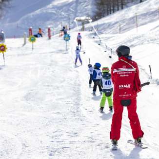 Un moniteur de ski accompagne les enfants sur le téléski d'entraînement de Malbun - domaine skiable idéal pour les familles et les débutants au Liechtenstein.