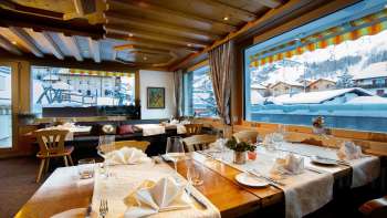 Salle de restaurant claire et accueillante avec une grande baie vitrée et vue sur les montagnes enneigées