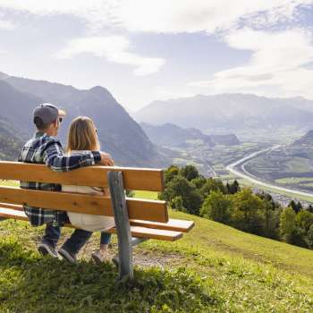 Deux randonneurs sont assis sur un banc et profitent de la vue sur la vallée du Rhin.
