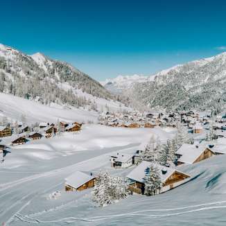 Vue aérienne de Malbun en hiver avec des maisons en bois enneigées, intégrées dans le paysage alpin du Liechtenstein.