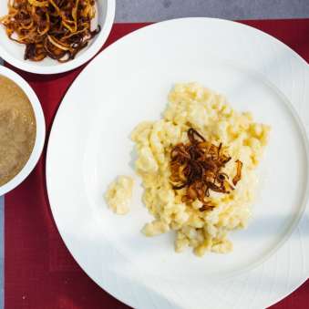 Käsknöpfle traditionnels avec oignons frits et compote de pommes du Liechtenstein sur assiette blanche