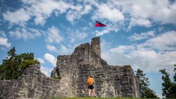 Randonneuse devant les ruines historiques du château de Schellenberg avec le drapeau du Liechtenstein flottant sous un ciel bleu