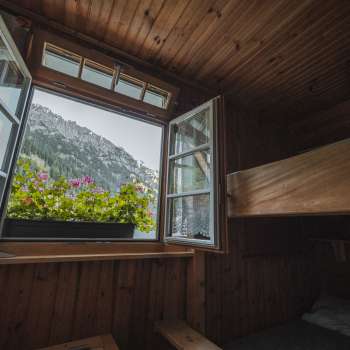 Vue de la fenêtre du dortoir : vue d'un dortoir simple avec lits superposés du refuge Gafadurahütte sur le paysage de montagne.