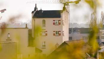 Gros plan sur la tour historique de l'hôtel de ville de Vaduz avec ses remarquables volets rouges, entourée de grues de chantier en arrière-plan.