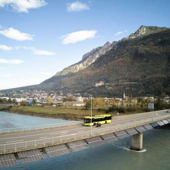 Un bus jaune LIEmobil traverse le pont sur le Rhin près de Vaduz avec un panorama de montagnes en arrière-plan - Découvrir le Liechtenstein