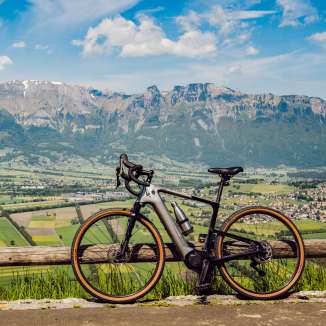 Vélo gravel appuyé contre la clôture ci-dessus Planken avec vue panoramique sur la vallée du Rhin et les Alpes du Liechtenstein – endroit idéal pour les cyclistes