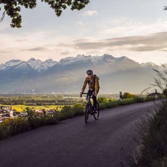 Cyclistes sur un sentier d'altitude panoramique avec vue sur la vallée du Rhin et les Alpes dans la lumière du soir - Aventure en Gravelbike au Liechtenstein