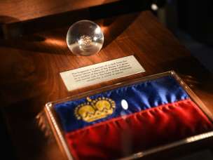 Pièce d'exposition dans le Trésor du Liechtenstein : drapeau du Liechtenstein avec couronne dorée et sphère en verre avec pièce historique trouvée