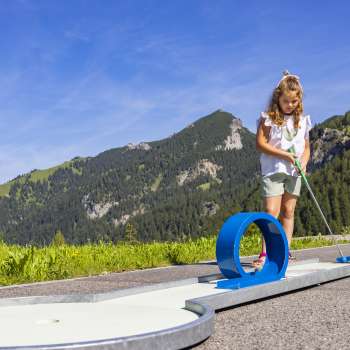 Une jeune fille se concentre sur une piste de looping bleue dans un décor alpin en jouant au mini-golf.
