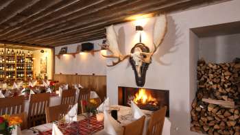 Ambiance chaleureuse du restaurant avec des poutres en bois rustiques, des nappes blanches et une cheminée crépitante.