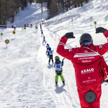 Cours de ski au Malbi-Park à Malbun avec des casques colorés et des moniteurs engagés - apprendre en toute sécurité dans un environnement adapté aux enfants.