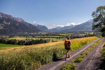 Une femme se promène sur un chemin de terre avec une vue panoramique sur la vallée du Rhin au Liechtenstein