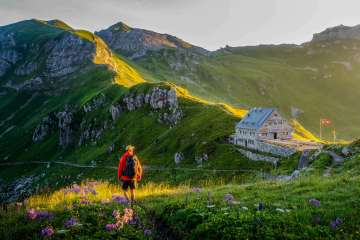 Un randonneur regarde le refuge Pfälzer au Liechtenstein, entouré d'un paysage de montagnes verdoyantes et d'un panorama alpin au crépuscule.