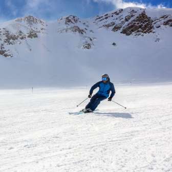Skieurs sur une large piste de ski à Malbun, Liechtenstein, entourés de pentes alpines enneigées et d'un ciel bleu éclatant