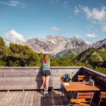 Une randonneuse contemple un impressionnant panorama alpin depuis une terrasse en bois près de la terrasse panoramique.