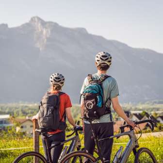 Deux cyclistes avec casque et sac à dos se tiennent à côté de leurs gravelbikes et contemplent l'imposant panorama alpin - le plaisir du vélo et la communion avec la nature au Liechtenstein
