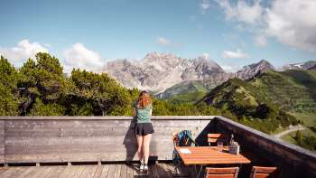 Une femme admire la vue sur les Alpes liechtensteinoises et la vallée du Rhin depuis la terrasse panoramique de Sareis par temps clair.