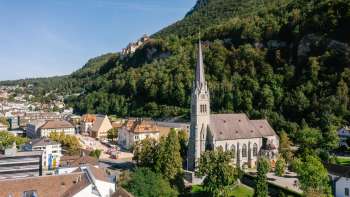 Vue aérienne de la cathédrale Saint-Florin à Vaduz avec le château de Vaduz en arrière-plan, par une journée ensoleillée.