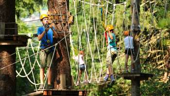 Enfants casqués et sécurisés traversant un pont suspendu dans un parc aventure Enfants casqués et sécurisés traversant un pont suspendu dans un parc aventure