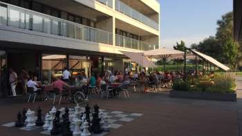 Terrasse ensoleillée bien fréquentée d'un restaurant moderne avec un grand terrain d'échecs à l'extérieur