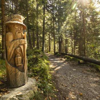 Figurine en bois avec lanterne au « sentier des légendes walsers » dans la lumière mystique de la forêt