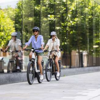 Deux femmes sur des vélos électriques traversent le centre moderne de Vaduz au Liechtenstein, avec sa façade en verre et son ambiance urbaine.