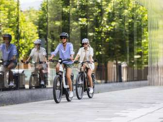 Deux femmes sur des vélos électriques traversent le centre moderne de Vaduz au Liechtenstein, avec sa façade en verre et son ambiance urbaine.