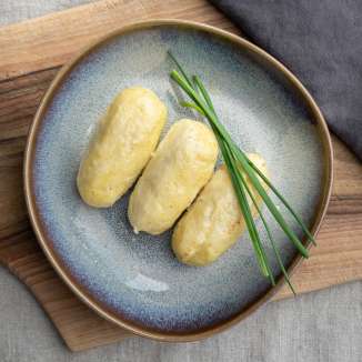 Trois boulettes de Hafalääb sur une assiette garnie de ciboulette, servies sur une planche en bois - plat traditionnel du Liechtenstein