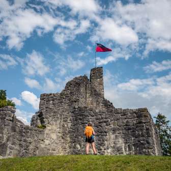 Randonneuse devant les ruines historiques du château de Schellenberg avec le drapeau du Liechtenstein flottant sous un ciel bleu